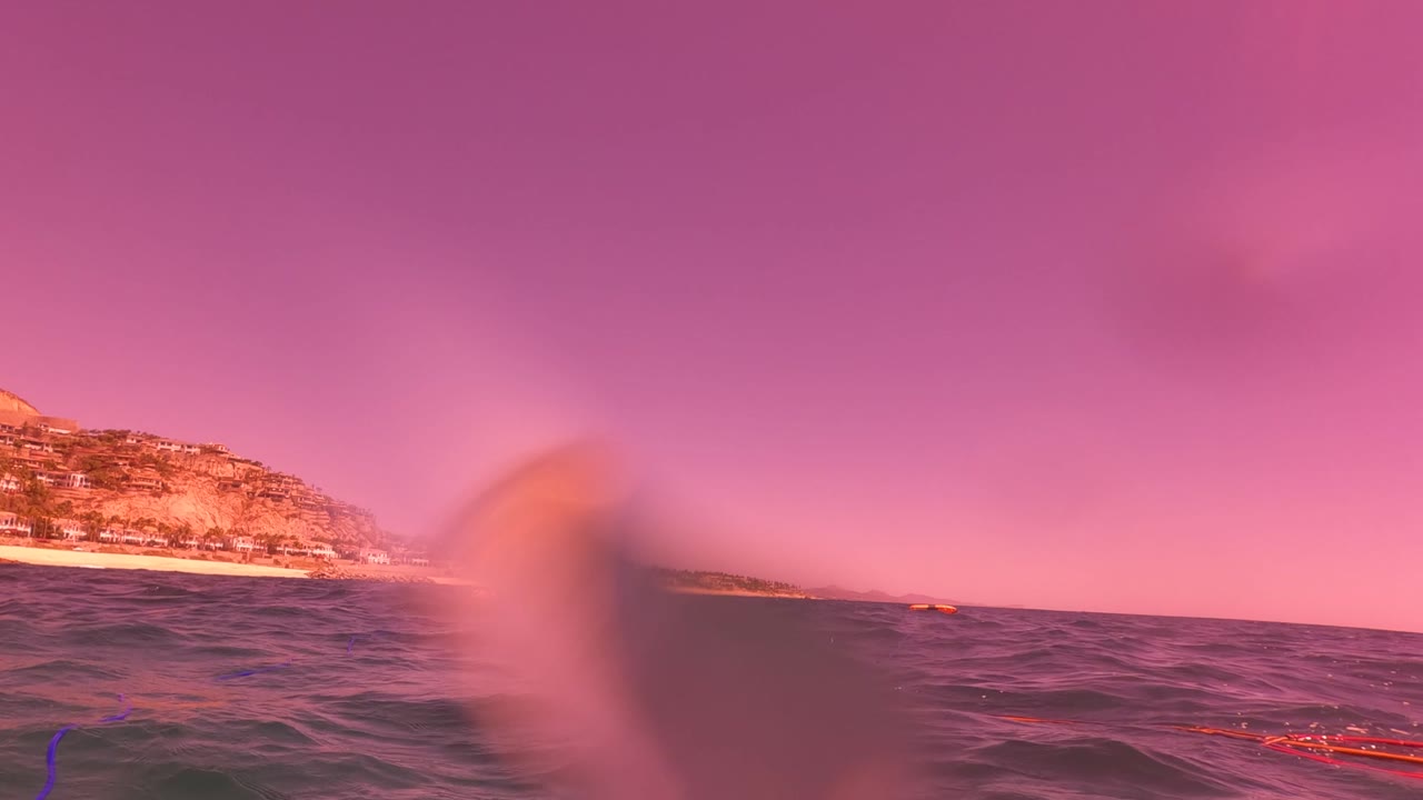 Ocean horizon with coastal buildings under a pink sunset sky.