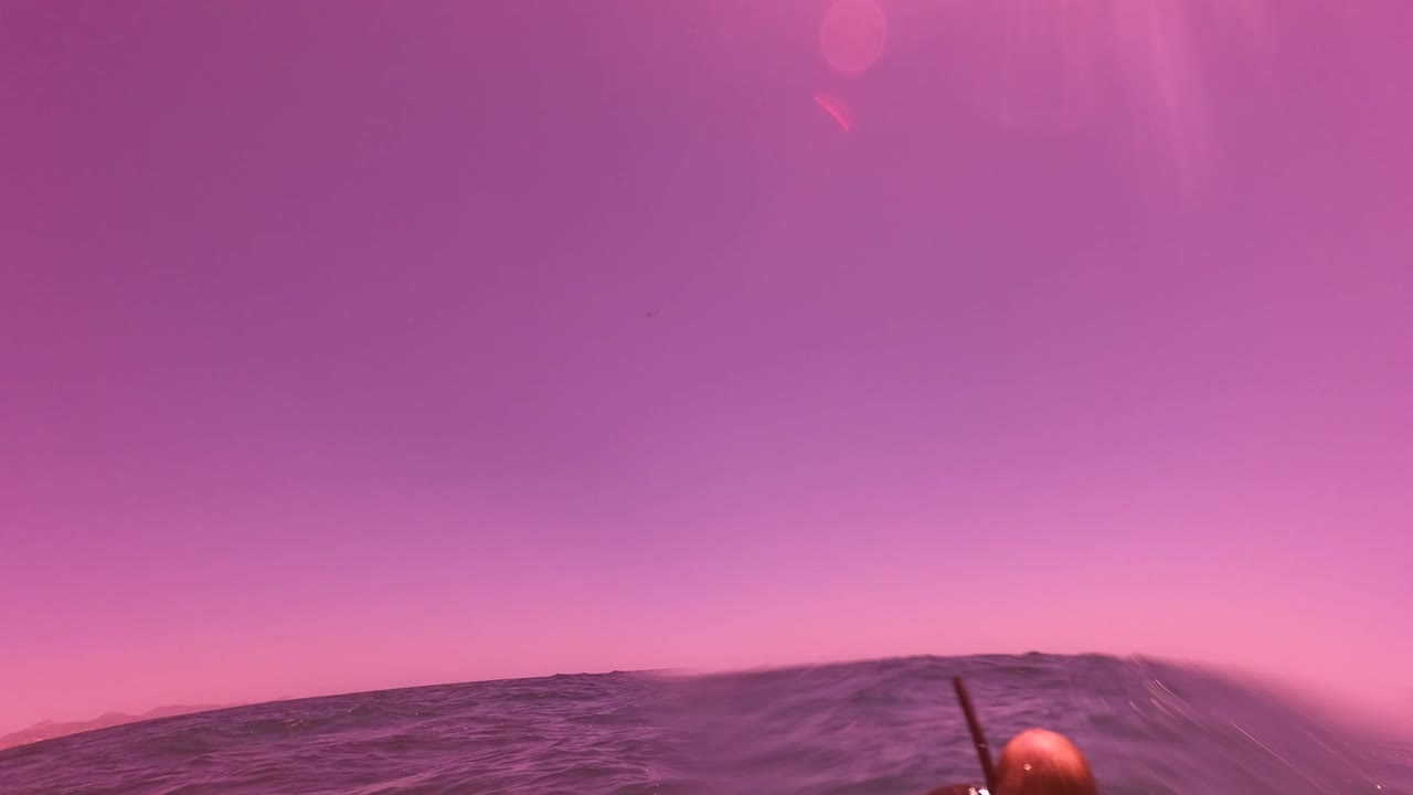 Water-level view in San Jose del Cabo shows purple ocean waves, a pink sky, and part of a snorkeler's head and snorkel at the lower right edge.