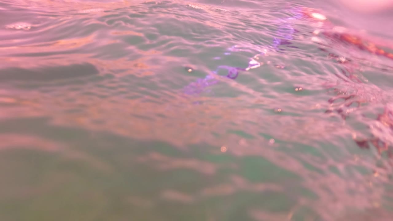Close water surface with pink reflections and ripples.