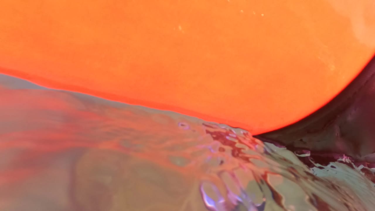 Orange surfboard edge pressed close to the lens at the water surface in San Jose del Cabo, with warm orange light, rippled water, a faint horizon, and no visible people.