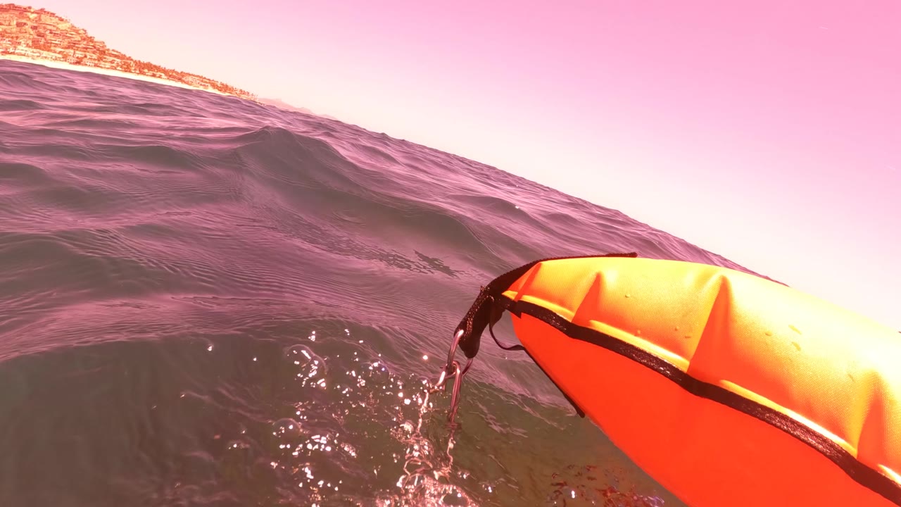 Orange surfboard tip floats at the right side of the frame in San Jose del Cabo, with choppy surface water, a low horizon, warm pink-orange sky color, and no visible people.