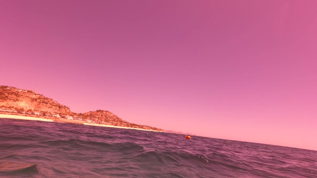 Choppy water fills the foreground while the beach and low hills sit along the horizon in San Jose del Cabo, with no visible people.