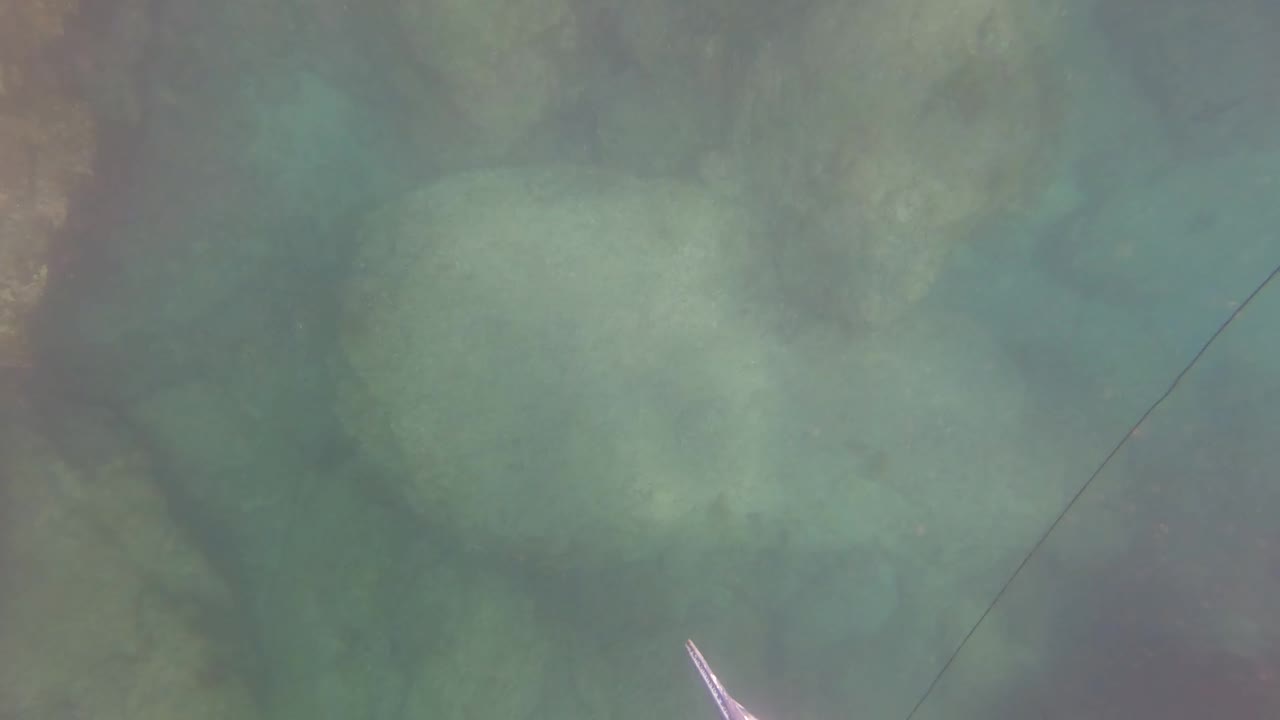 Clear underwater rock bed in San Jose del Cabo with the fishing line running diagonally and a pale lure or fish-like form near the lower left, with no visible people.