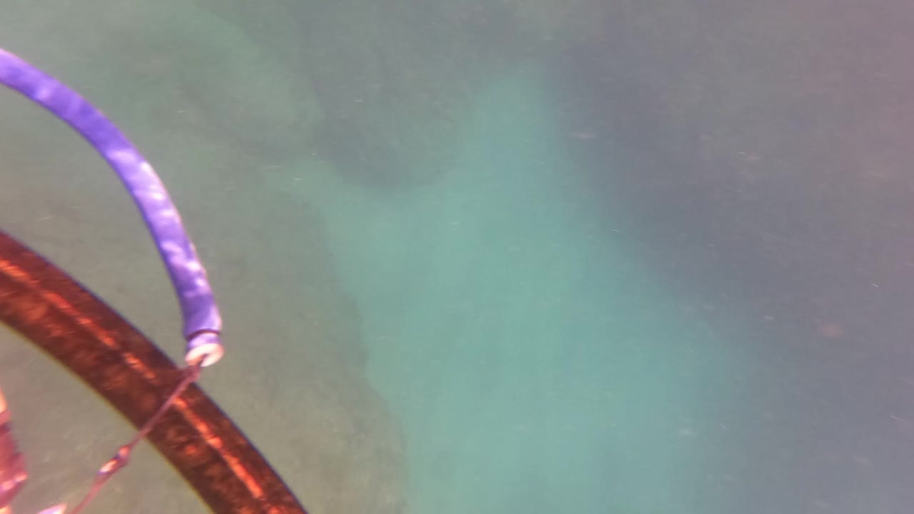 San Jose del Cabo underwater frame with a purple curved tube, rope, and brown boat-related element crossing above a rocky seabed with no visible people.