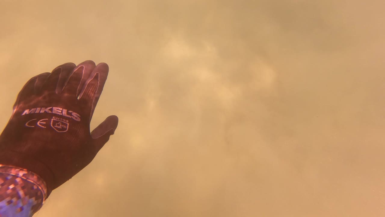 A dark gloved hand enters from the left edge against a yellow hazy sky in San Jose del Cabo, with no visible face.