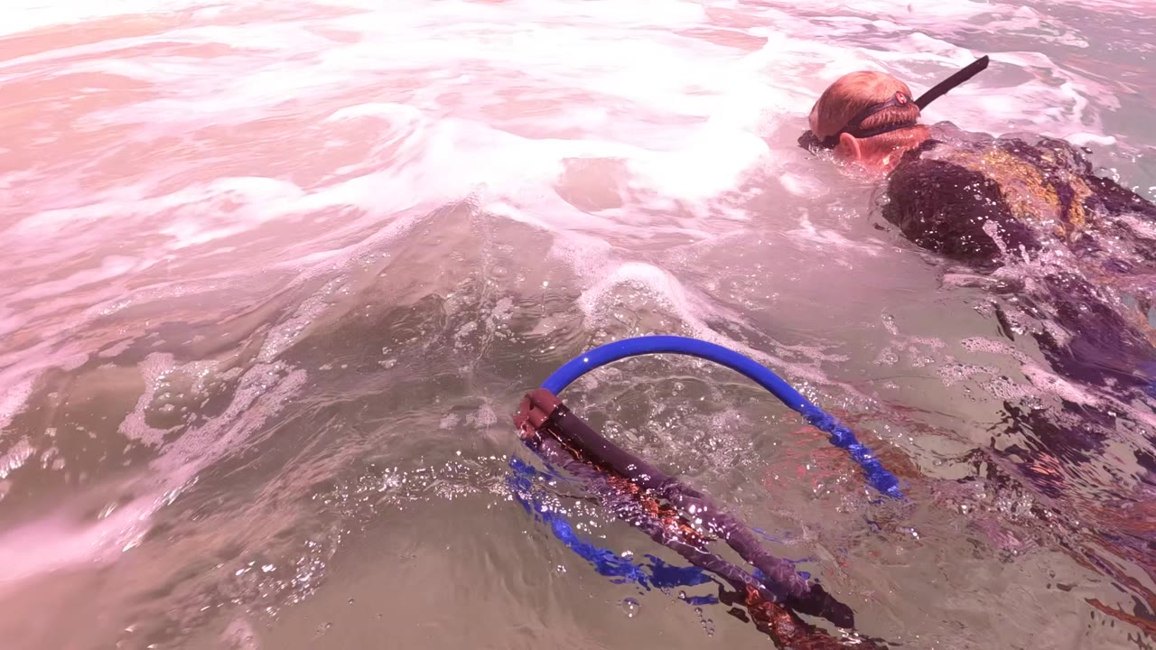 At San Jose Del Cabo, Baja California Sur, a surfer or swimmer is partly above foamy water while blue ring gear sits close to the lens in the foreground.
