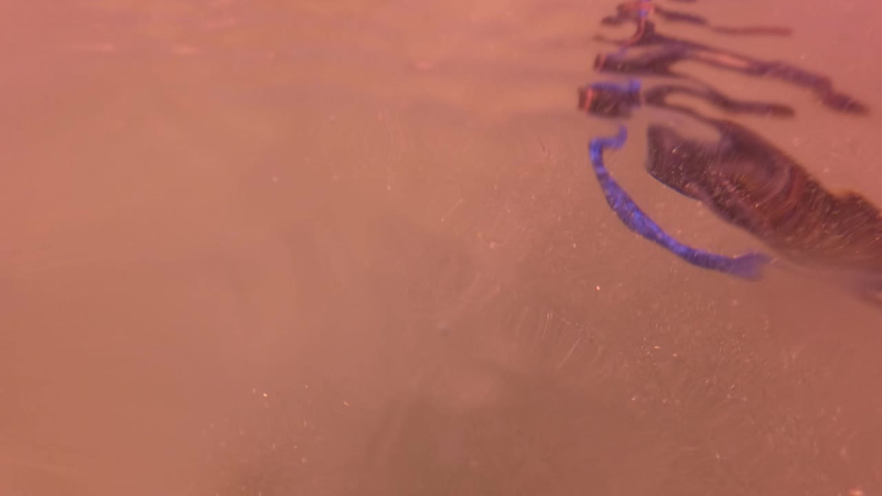 Close overhead pink water surface in San Jose del Cabo with blurred dark reflections, blue curved reflection, and light foam across the frame.