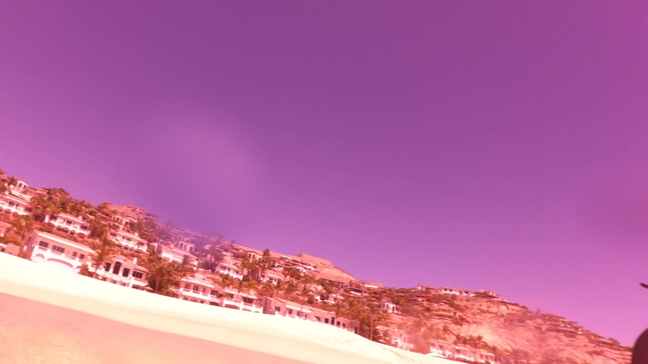 Tilted beach view with hillside buildings under a pink-purple sky.