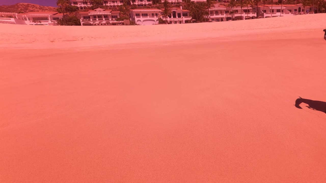 Sandy beach with distant buildings and a small dark figure near the upper right.