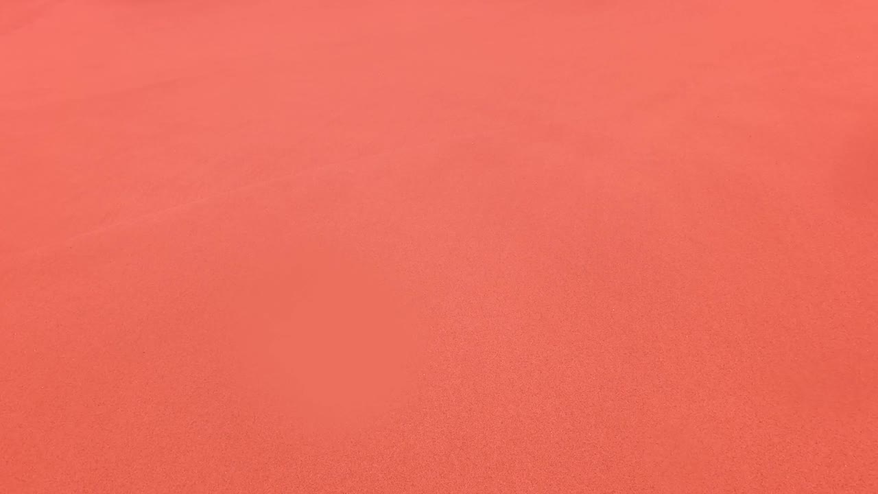 Open pink-orange beach sand in San Jose Del Cabo with only a thin line of distant shoreline detail and no clear person visible in frame.
