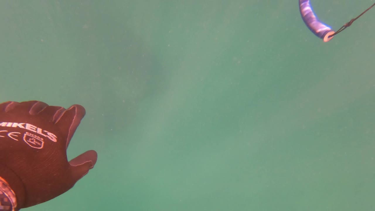 Gloved hand underwater near a kite control bar and line.