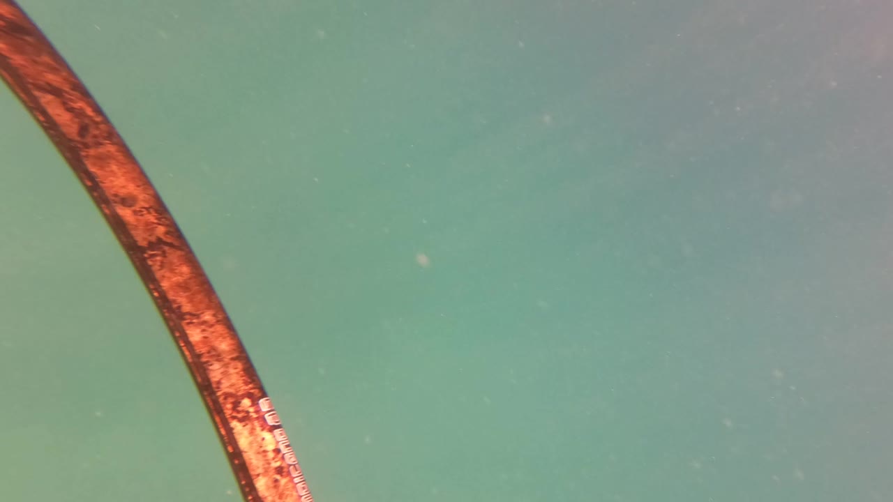 Close underwater view of a rusted pipe cutting through green-blue water in San Jose del Cabo, with suspended particles and no visible people.