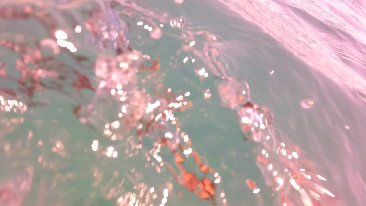 Close water surface with bubbles, ripples, and pink reflections