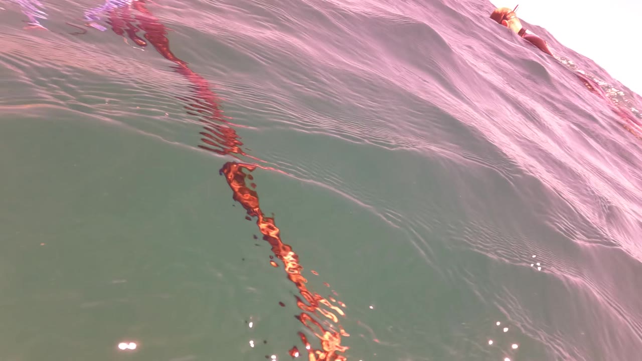 Rippled ocean surface in San Jose del Cabo with pink reflections and a small piece of fishing or kiteboarding gear near the top edge, with no visible people.