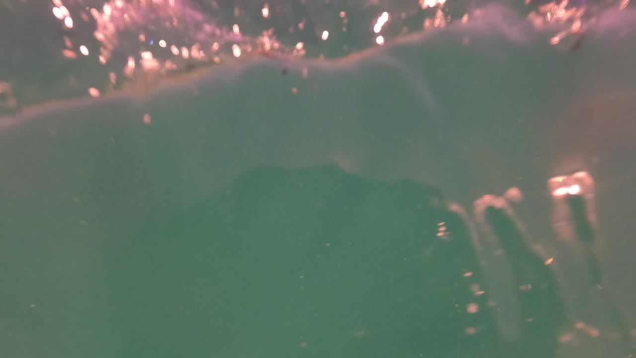 Partial underwater view with green water and bright bubbles near the surface.