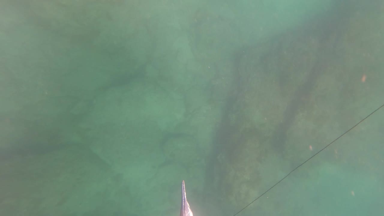 The San Jose Del Cabo underwater view shows soft green water, submerged rocks, a faint diagonal line, and a pointed tool tip rising from the lower edge, with no visible people.