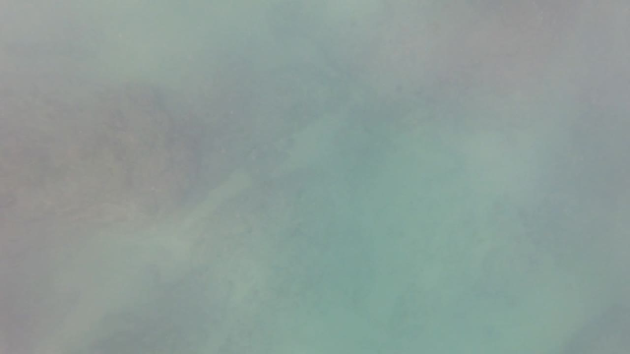 Cloudy turquoise water in San Jose del Cabo with indistinct darker rock or coral patches and no visible people.