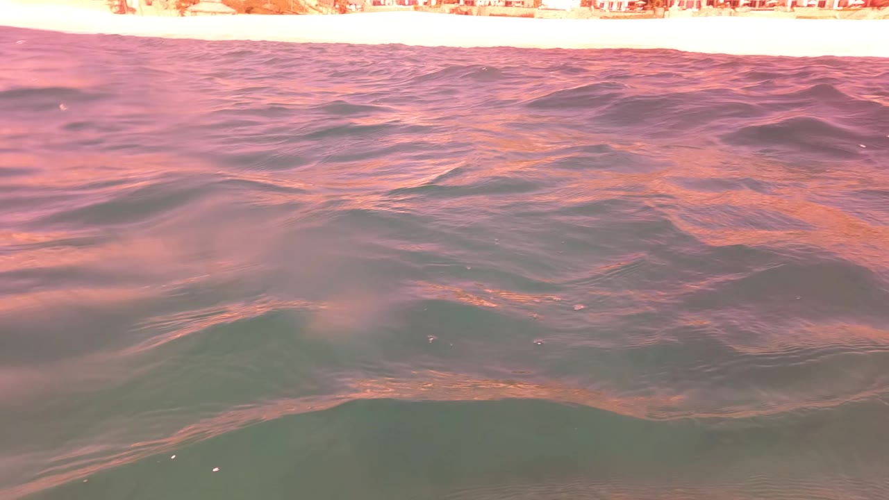 Pink-lit ocean surface with a narrow shoreline strip.