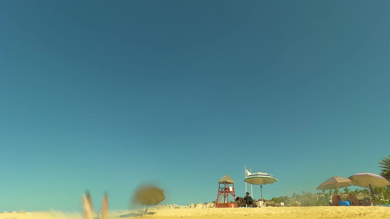Low waterline view of beach umbrellas and lifeguard tower under blue sky