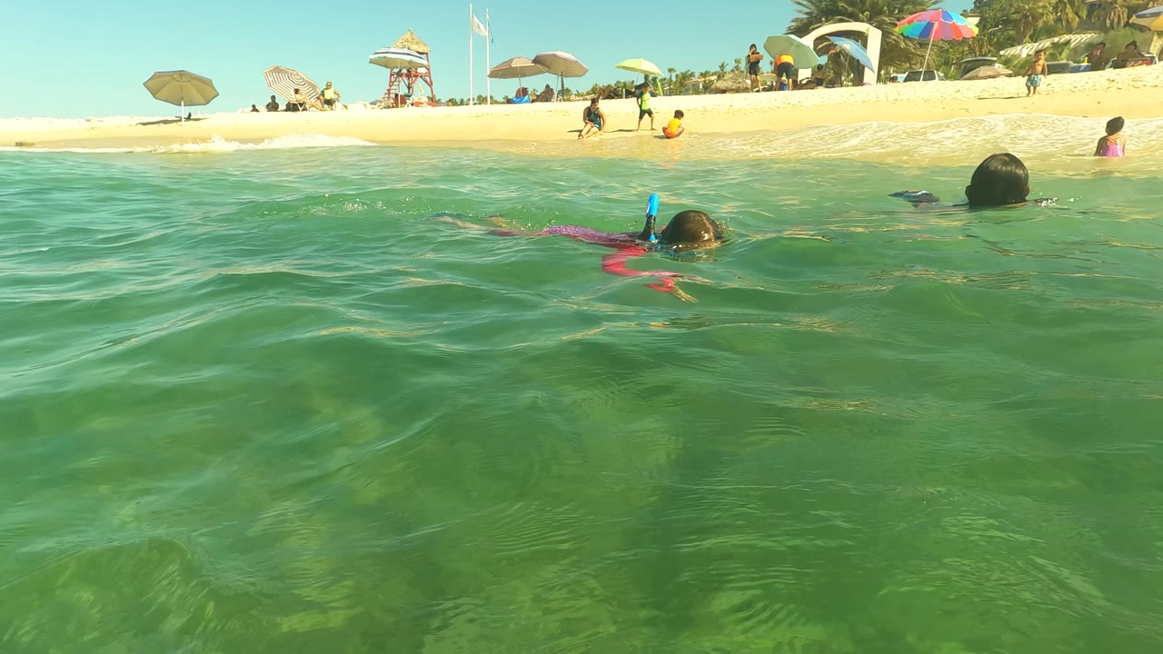 Snorkeler closer to center with beach umbrellas and swimmers behind