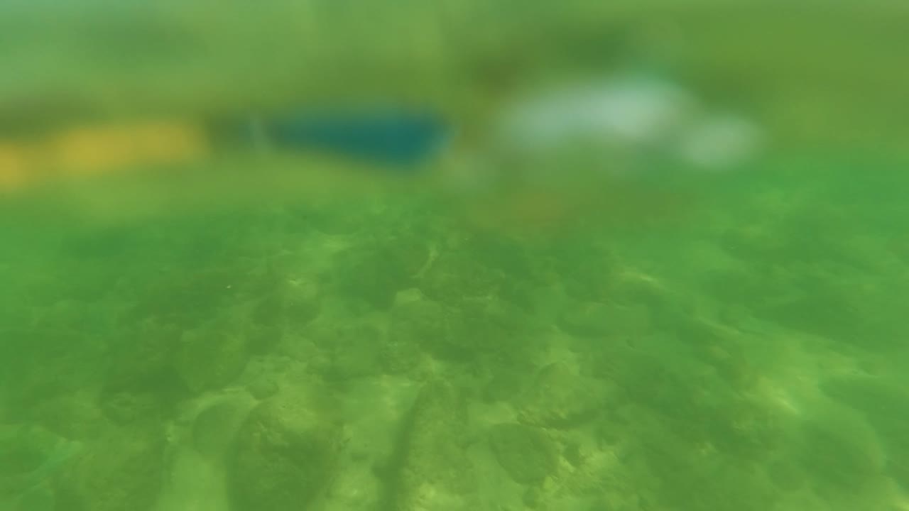 The view is partly submerged in San Jose del Cabo, showing green water, blurred rocks below, and a soft surface line with no visible people.