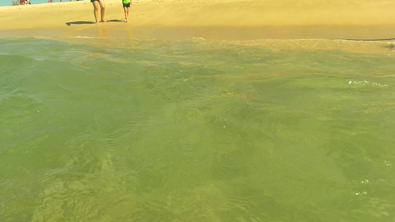 At San Jose del Cabo, two beachgoers stand near the shore in the background while clear green water fills most of the frame.