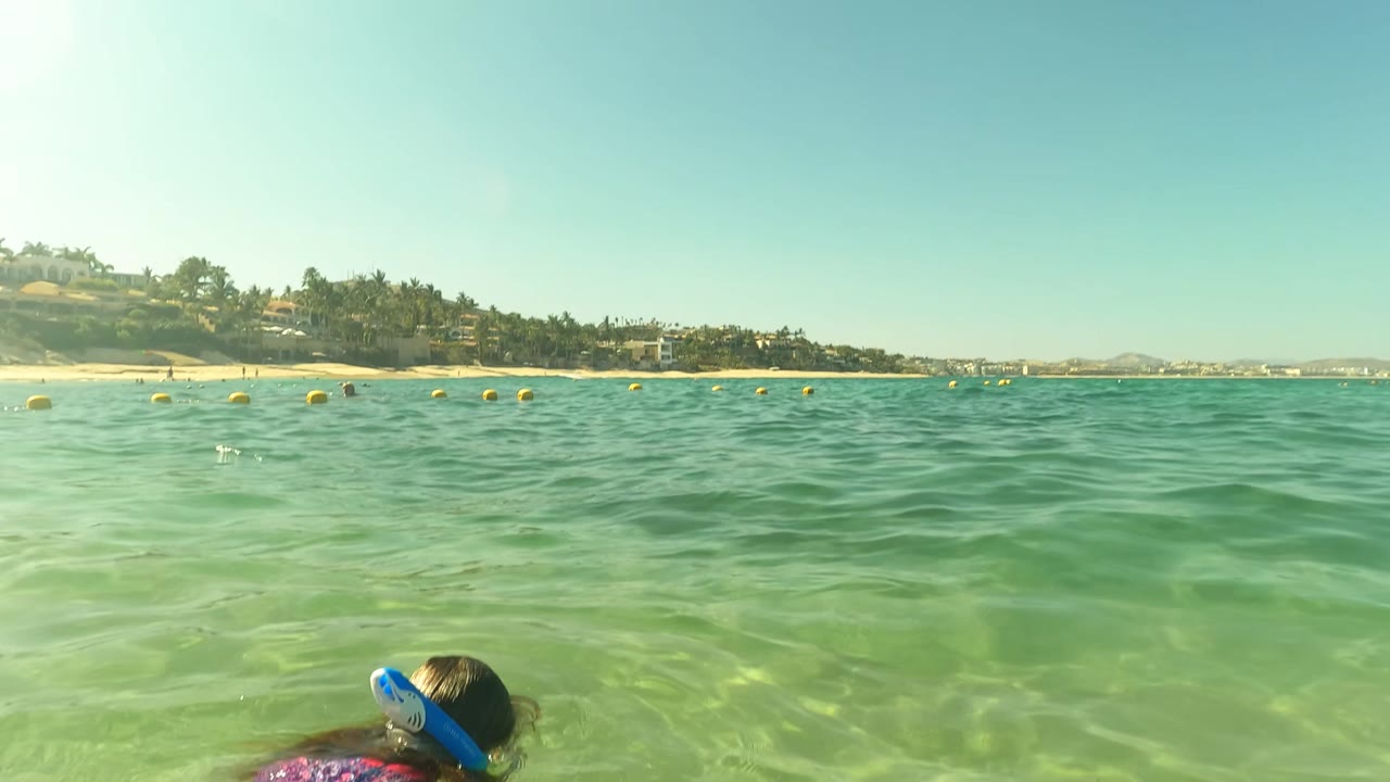 Snorkeler at the edge of clear ocean water near beach buoys
