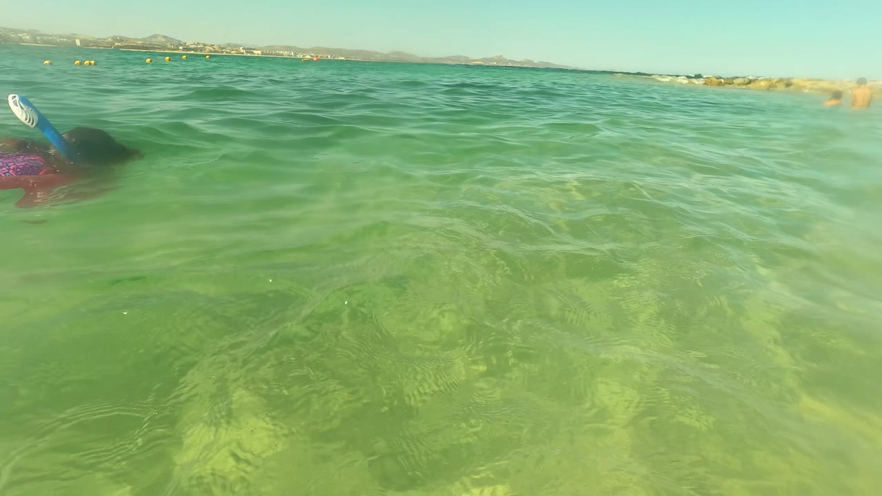 The snorkeler is partly submerged beneath rippled green water in San Jose Del Cabo, with a blue snorkel or fin visible and the horizon low across the top of the frame.