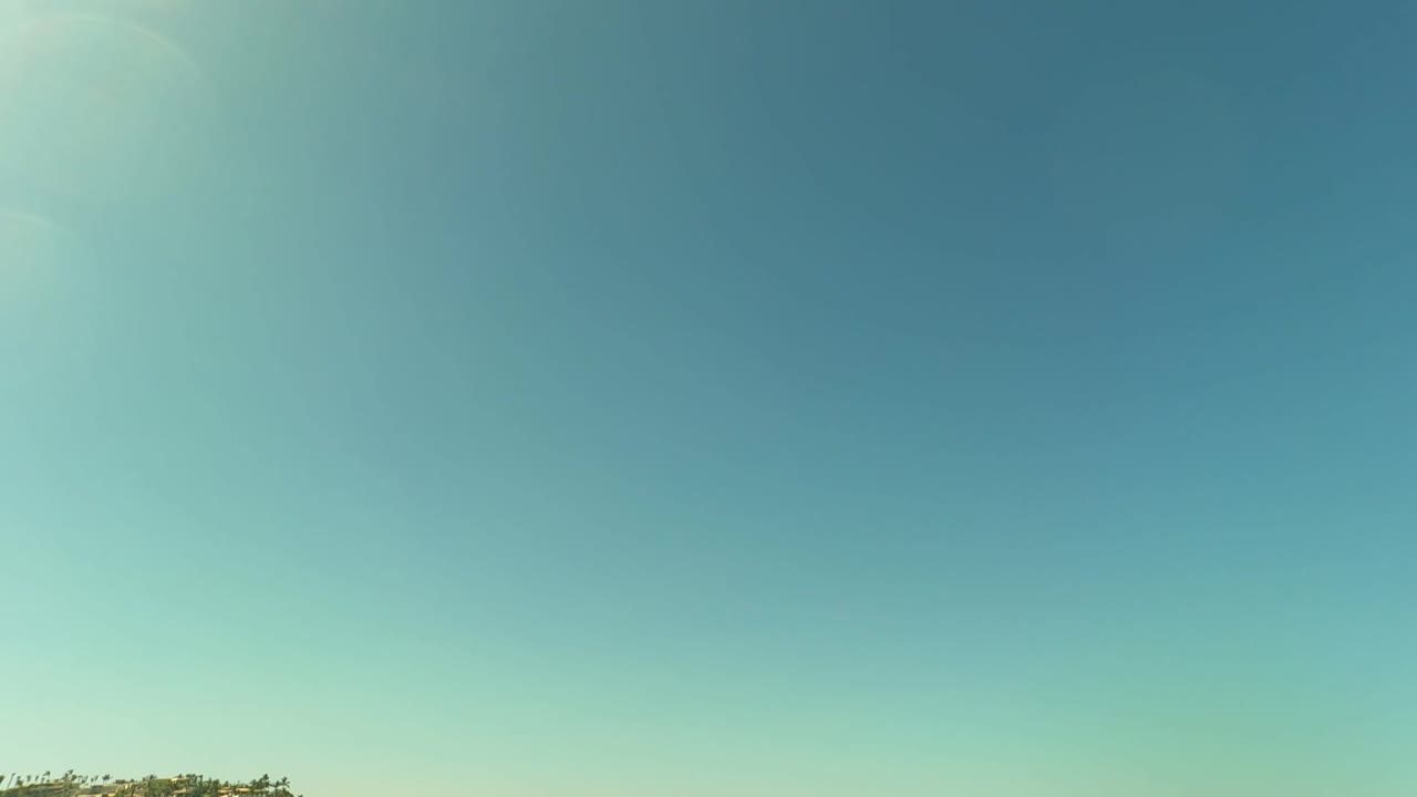 Opening frame in San Jose Del Cabo shows mostly clear blue sky with a thin strip of shoreline at the lower edge and no visible people.