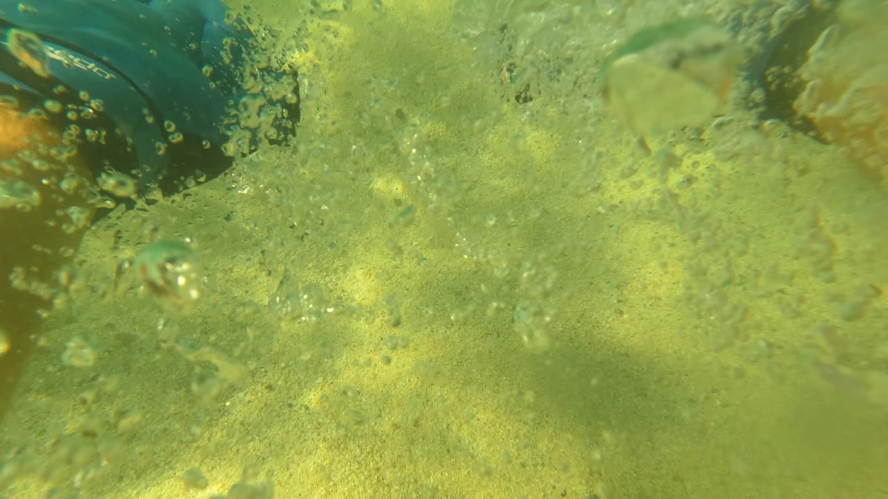 Close underwater view of swimmer legs, blue flipper, and bubbles.
