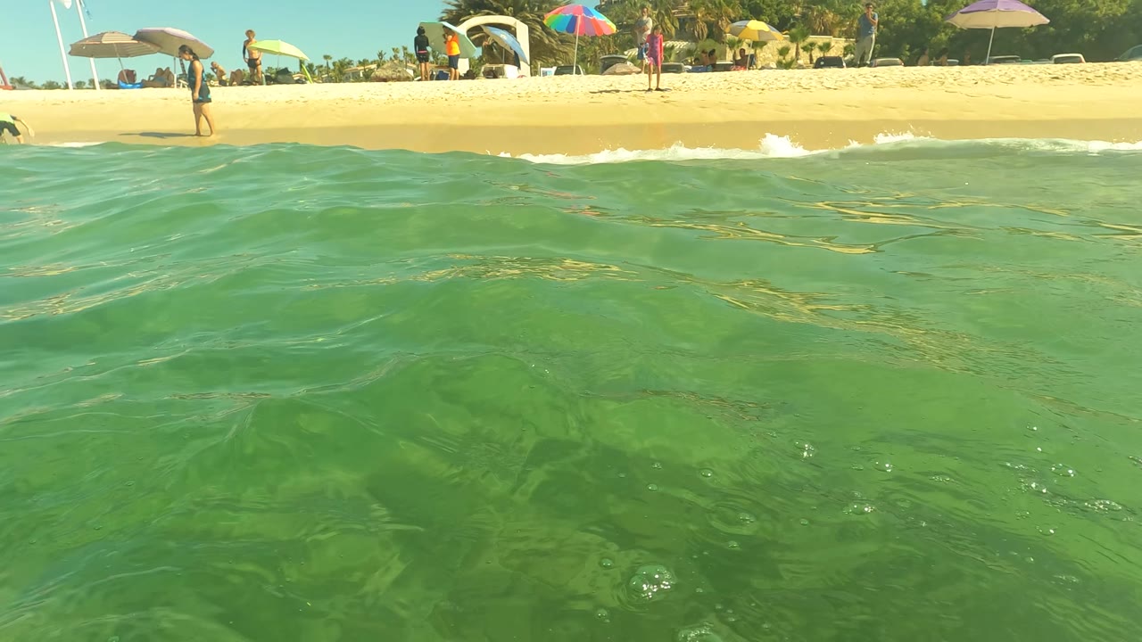 Low ocean view toward a sandy beach with umbrellas and gentle shore break.