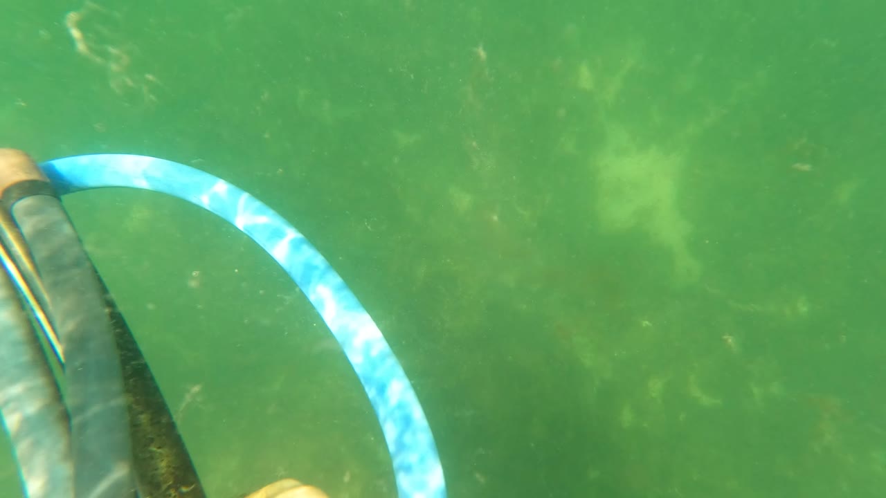 At 0:03 in San Jose del Cabo, Baja California Sur, Mexico, the blue striped hose loops through the frame beside a dark grip and partial hand over algae-softened green bottom.