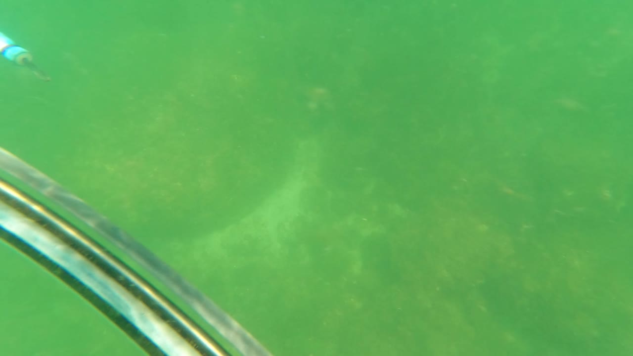 A metal boat structure angles through the foreground underwater in San Jose del Cabo, with green water, seabed texture, and no visible people.
