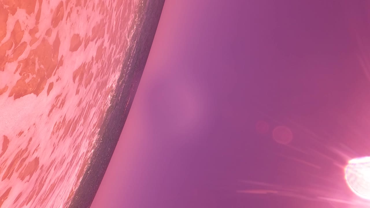 Foamy pink water fills the left side while a dark seawall edge cuts diagonally across a purple glare field in San Jose Del Cabo, with no visible people.