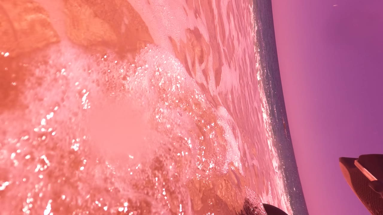 Pink surf foam fills the foreground near the camera while the seawall edge and purple light field recede through the frame in San Jose Del Cabo, with no visible people.