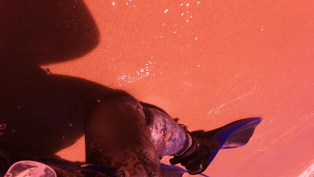 Cropped legs in camouflage pants beside pink water and blue gear.