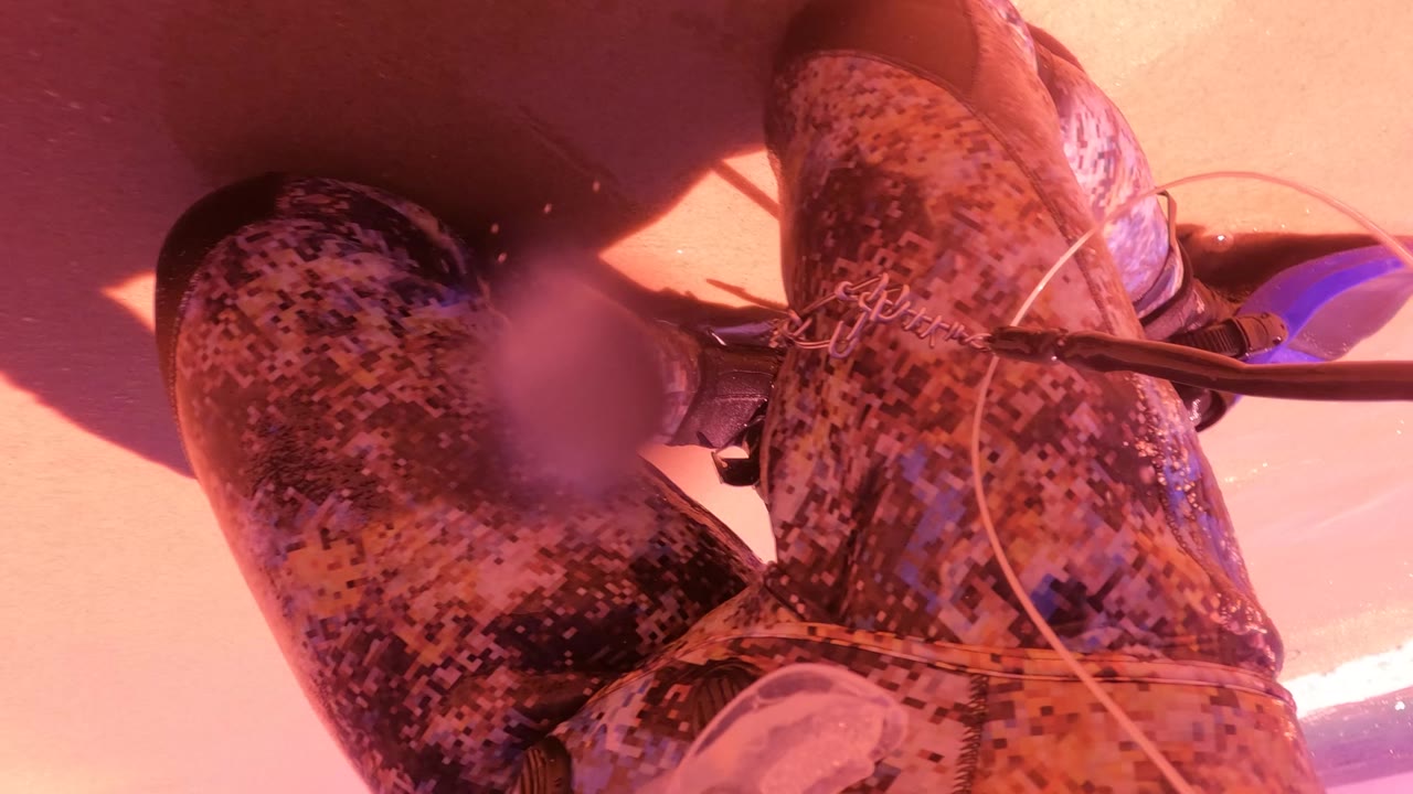 The rider's camo legs, clear tubing or line, and blue gear fill the frame above pink salt water in San Jose Del Cabo, with the body cropped so no face is visible.