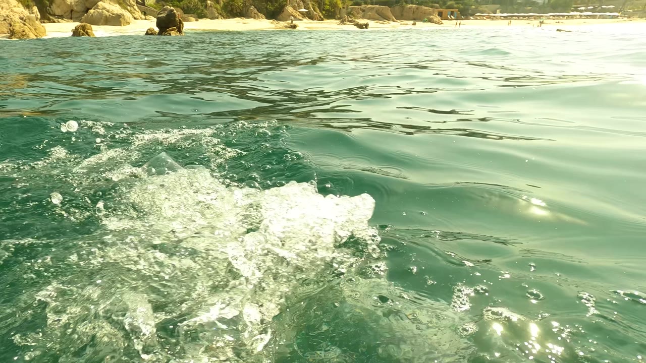 Foam breaks across green ocean water near a rocky shoreline in San Jose del Cabo, Mexico, with no visible people in the foreground water.