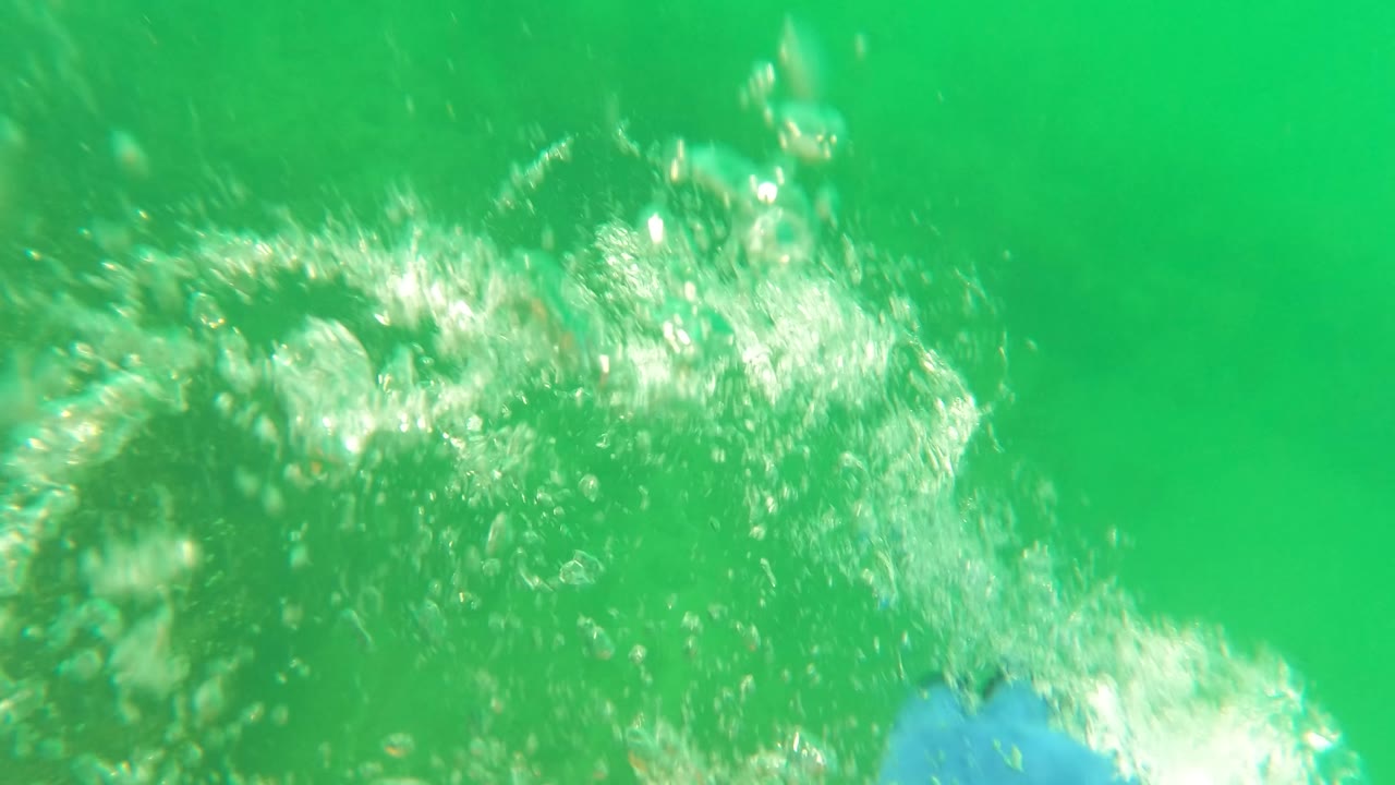 A bright cluster of bubbles rises through green water in San Jose Del Cabo above dim seabed texture, with no visible people.
