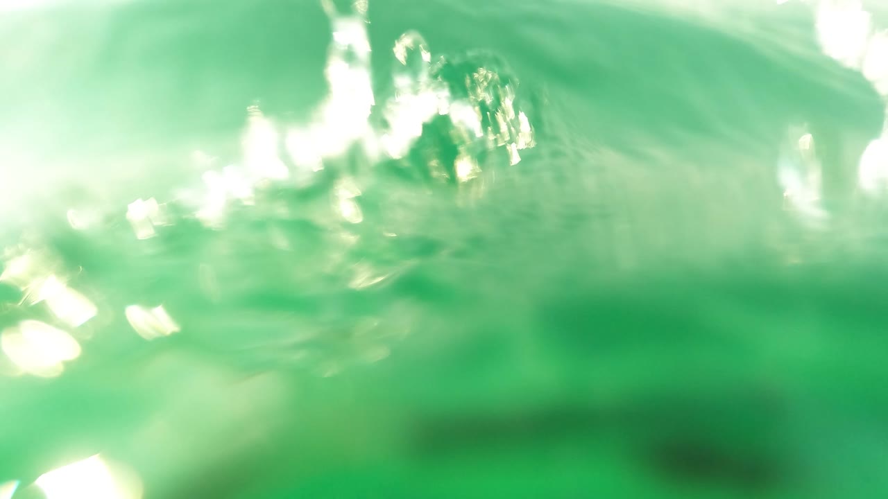 Half-submerged view with bright sun reflections and blurred green water.