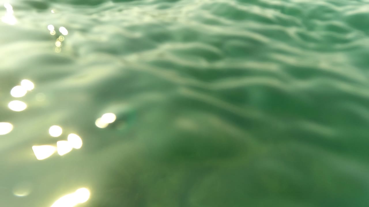 Rippling water surface and bright sun reflections sit above a dim reef shape in San Jose Del Cabo, with no visible people.