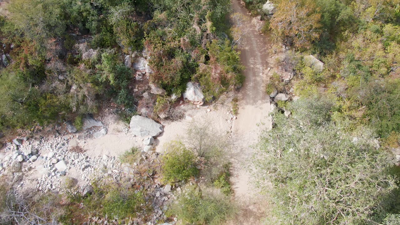 Aerial frame over San Dionisio, Baja California Sur with the dirt trail near the top of frame and a pale rocky wash and shrubs below, with no visible people.