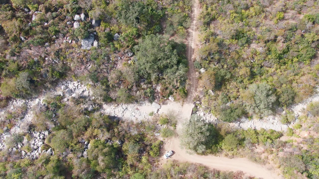 White vehicle on a winding dirt road through scrub and rocks.
