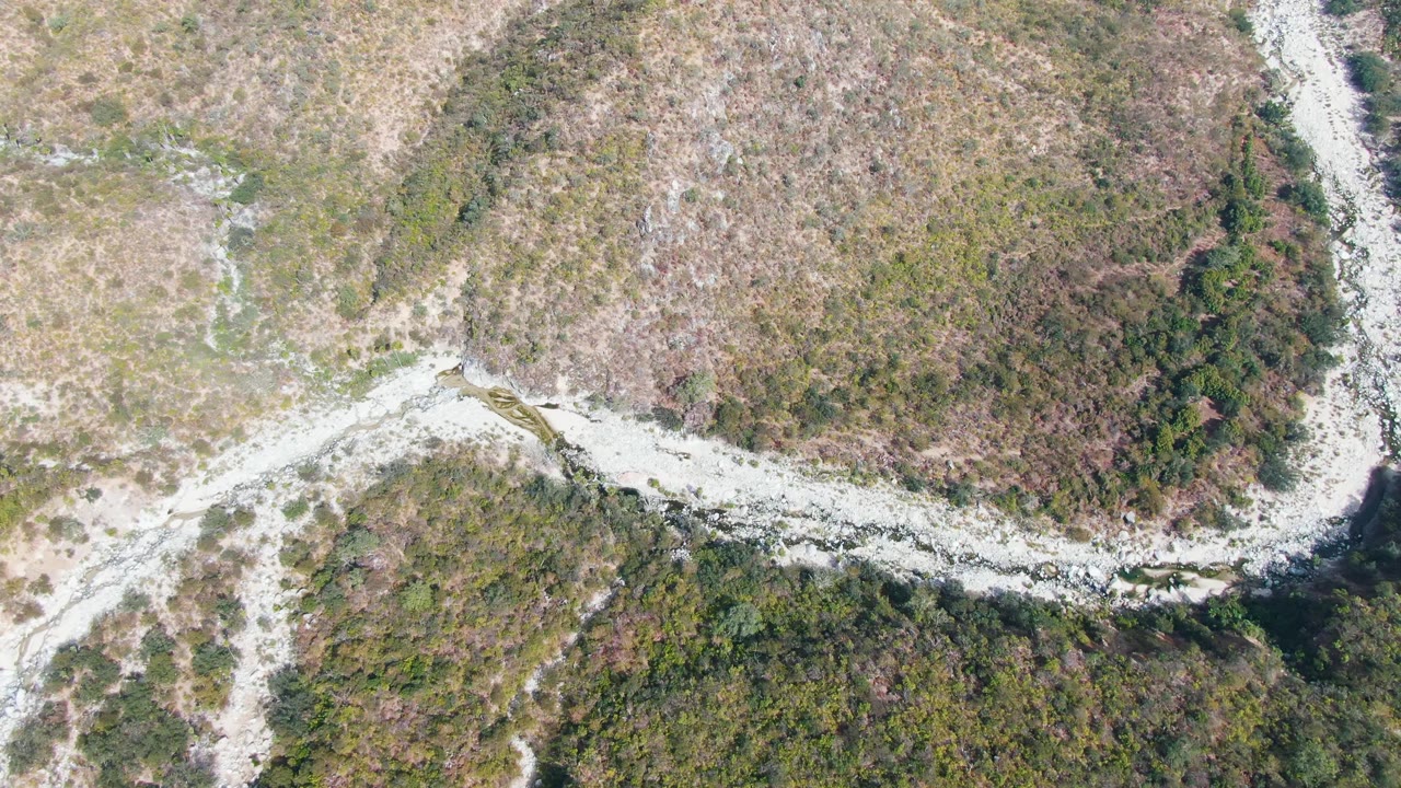 Aerial frame over San Dionisio, Baja California Sur showing a pale dirt road curving through green and brown scrubland with denser vegetation below and no visible people.