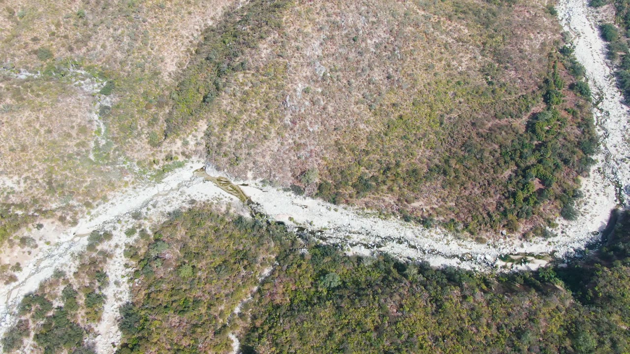 Overhead view in San Dionisio, Baja California Sur with the pale road bending across the center, dry hillside above, darker vegetation below, and no visible people.