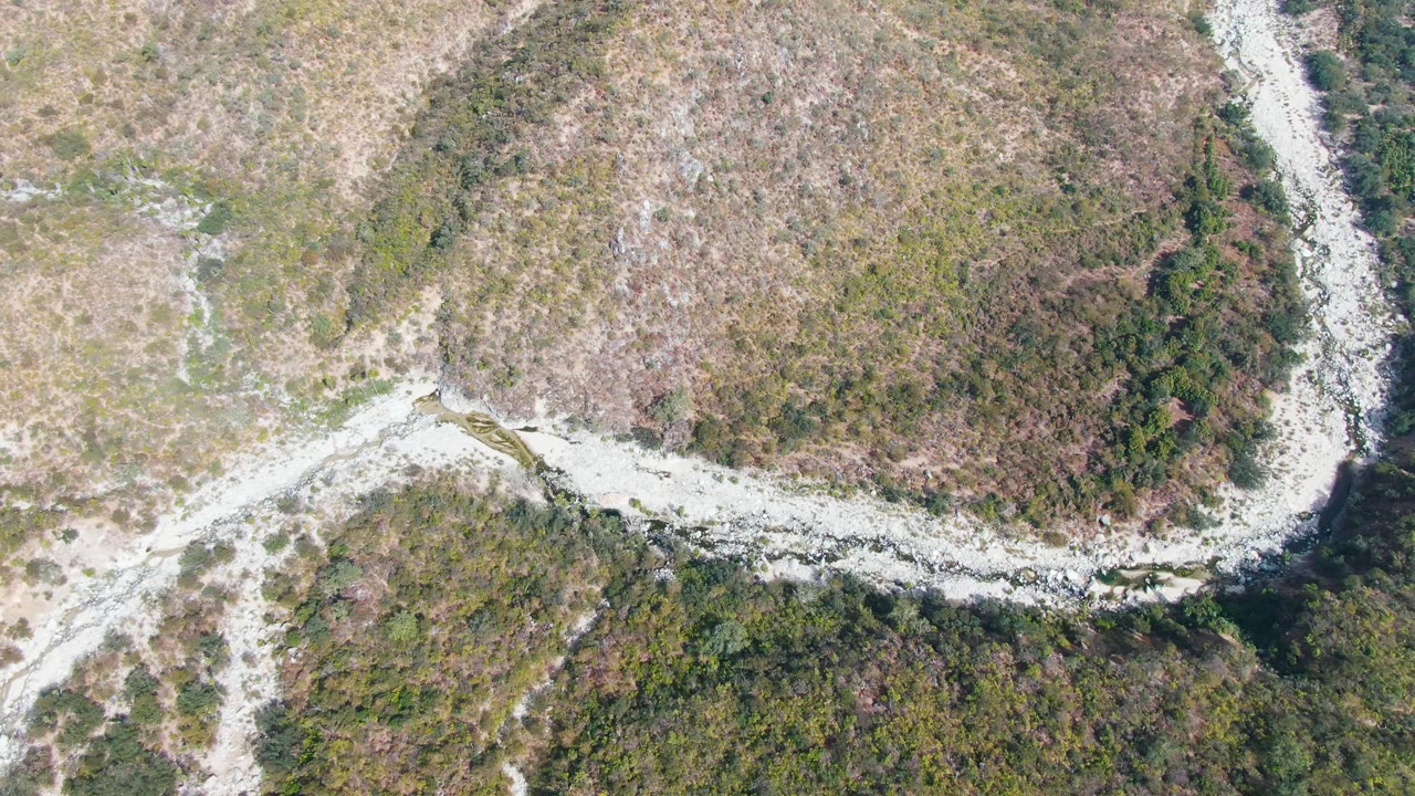 Top-down view of a winding pale road beside a dark ravine edge