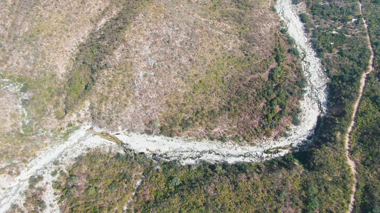 Aerial frame from San Dionisio, Baja California Sur, showing the pale winding stream beside a darker green vegetation corridor and no visible people.