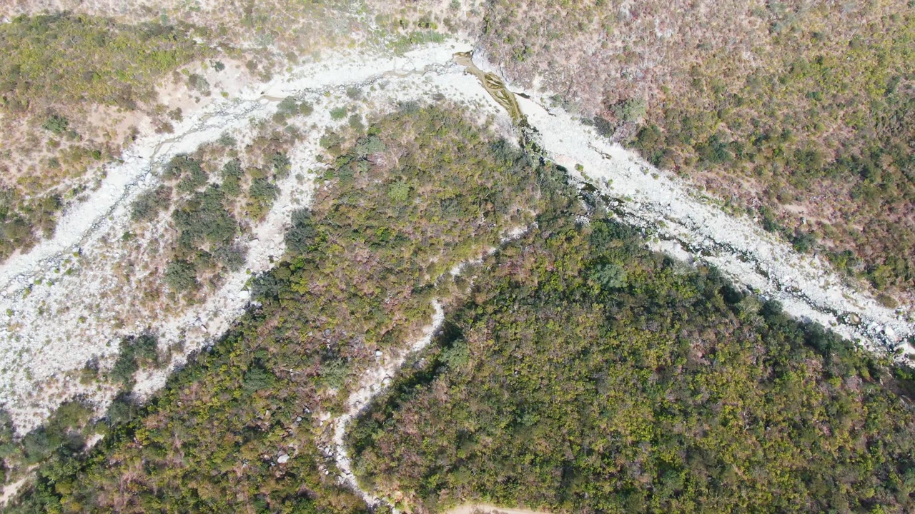 Top-down view in San Dionisio, Baja California Sur where a narrow mountain dirt path crosses exposed pale rock and patchy green vegetation, with no visible people.