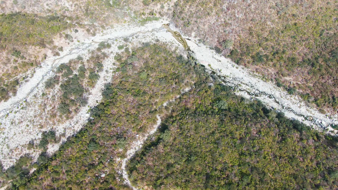 Aerial frame from San Dionisio, Baja California Sur showing the winding dirt track lower in the shot and a pale rocky wash above it, with no visible people.