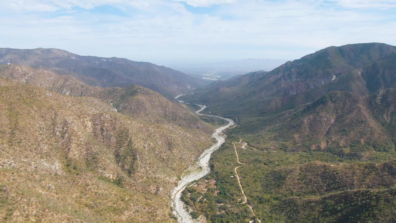 Aerial view of river, valley vegetation, and rocky mountains.